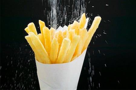 Sprinkling salt on chips in paper cone Stock Photo - Premium Royalty-Free, Code: 659-01862146