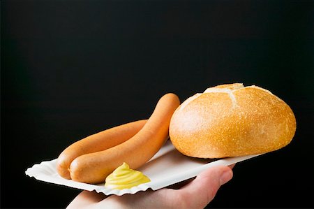 sausage, bun - Hand holding frankfurters, roll & mustard on paper plate Stock Photo - Premium Royalty-Free, Code: 659-01862280