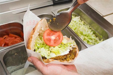 snackbar - Adding tomato to pita bread filled with falafel Foto de stock - Sin royalties Premium, Código: 659-01862655