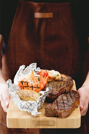 Man holding Surf & Turf (steaks & prawns) on chopping board Stock Photo - Premium Royalty-Free, Code: 659-01862830