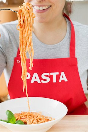 simsearch:659-01855701,k - Young woman in apron eating spaghetti with tomato sauce Stock Photo - Premium Royalty-Free, Code: 659-01863211