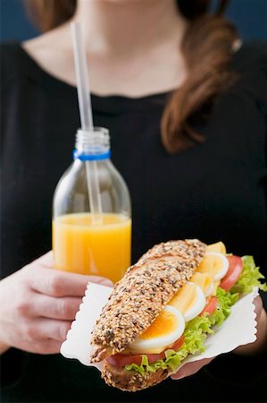 single sandwich - Woman holding sandwich and bottle of orange juice Stock Photo - Premium Royalty-Free, Code: 659-01863798