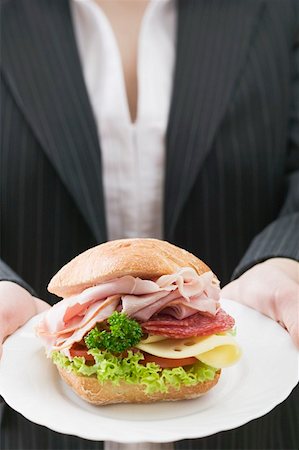 Woman holding a ham and cheese sandwich on a plate Stock Photo - Premium Royalty-Free, Code: 659-01863801
