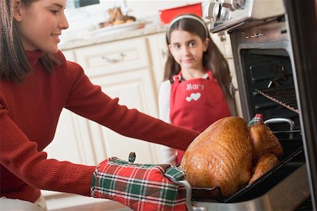 Woman taking turkey out of oven, girl in background Stock Photo - Premium Royalty-Free, Code: 659-02214241