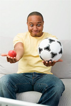 Young man with apple and football watching TV Stock Photo - Premium Royalty-Free, Code: 659-02211469