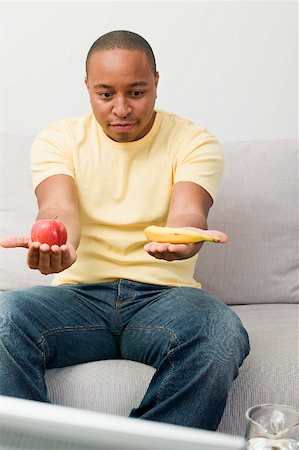 Young man with apple and banana watching TV Stock Photo - Premium Royalty-Free, Code: 659-02211470