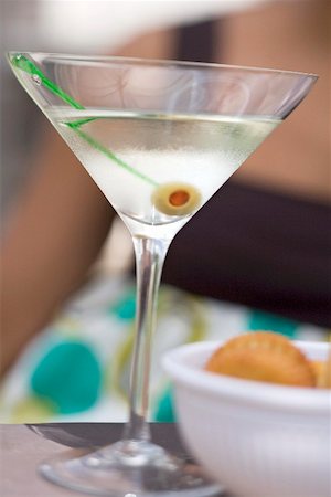 Martini with green olive, crackers, woman in background Stock Photo - Premium Royalty-Free, Code: 659-02211773