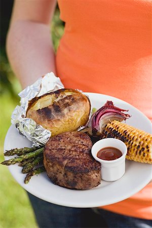 simsearch:659-01863429,k - Woman holding a plate of grilled steak and accompaniments Stock Photo - Premium Royalty-Free, Code: 659-02211818