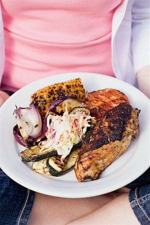 simsearch:659-03535955,k - Seated woman holding plate of grilled chicken breast & accompaniments Stock Photo - Premium Royalty-Free, Code: 659-02211825