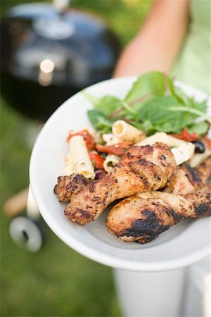 Woman holding plate of grilled chicken legs & pasta salad Stock Photo - Premium Royalty-Free, Code: 659-02211994