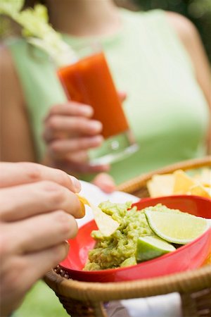 simsearch:659-03524301,k - Hand holding basket of guacamole & chips, woman with tomato drink Fotografie stock - Premium Royalty-Free, Codice: 659-02212094