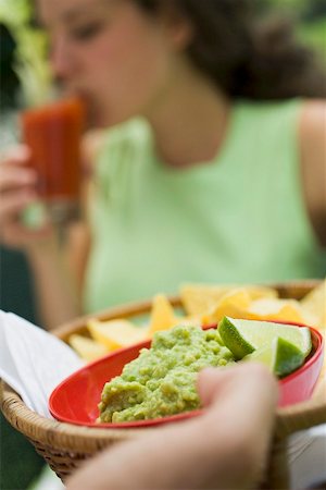 Hand holding basket of guacamole & chips, woman in background Stock Photo - Premium Royalty-Free, Code: 659-02212091