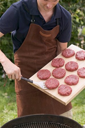 simsearch:659-01846050,k - Man lifting raw burgers from chopping board on to barbecue Stock Photo - Premium Royalty-Free, Code: 659-02212660