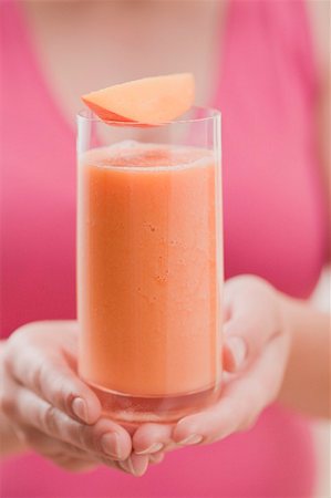 smoothy - Woman holding glass of mango smoothie with wedge of mango Stock Photo - Premium Royalty-Free, Code: 659-02213027