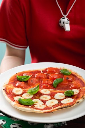 Female footballer holding tomato & mozzarella pizza with basil Stock Photo - Premium Royalty-Free, Code: 659-02213176