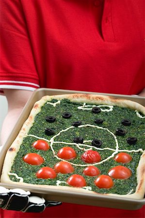 Female footballer holding spinach pizza with tomatoes & olives Stock Photo - Premium Royalty-Free, Code: 659-02213182