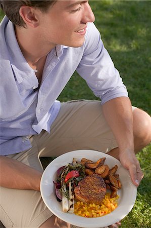 Young man holding a plate of grilled steak & accompaniments Stock Photo - Premium Royalty-Free, Code: 659-03524305