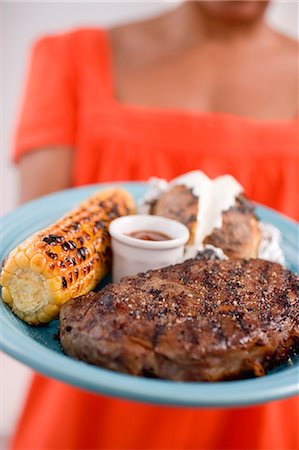 simsearch:659-07610088,k - Woman holding plate of steak, corn on the cob, baked potato Foto de stock - Sin royalties Premium, Código: 659-03524309