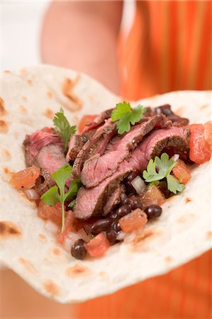 simsearch:659-03527105,k - Woman holding beef fajita with beans and tomatoes Foto de stock - Royalty Free Premium, Número: 659-03524531