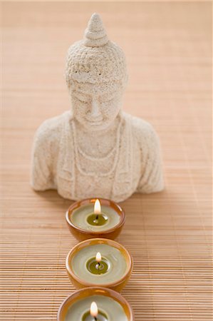 Three windlights in front of Buddha statue on bamboo mat Fotografie stock - Premium Royalty-Free, Codice: 659-03524650