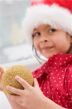 simsearch:659-03521663,k - Small girl in Father Christmas hat holding Christmas bauble Foto de stock - Sin royalties Premium, Código: 659-03525788