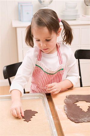 Small girl placing chocolate biscuit on baking tray Foto de stock - Sin royalties Premium, Código: 659-03526633