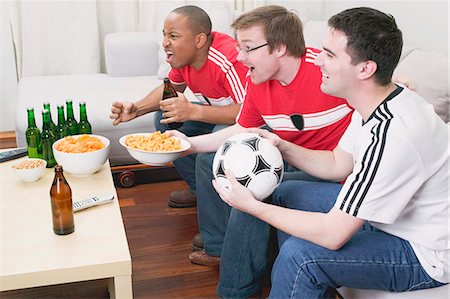 sitting on soccer ball - Three football fans with nibbles and beer watching TV Stock Photo - Premium Royalty-Free, Code: 659-03527332