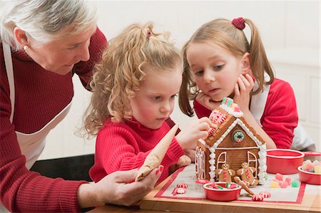 Small girls and grandmother decorating gingerbread house Stock Photo - Premium Royalty-Free, Code: 659-03528132