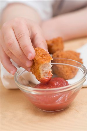 Child dipping chicken nugget in ketchup Stock Photo - Premium Royalty-Free, Code: 659-03528402