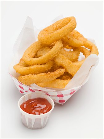 Deep-fried onion rings in paper dish, ketchup beside it Foto de stock - Royalty Free Premium, Número: 659-03529167