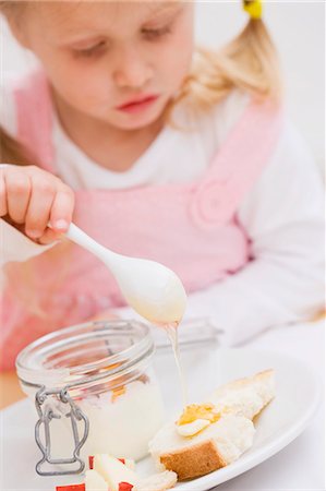 Little girl trickling honey onto bread and butter Stock Photo - Premium Royalty-Free, Code: 659-03529418