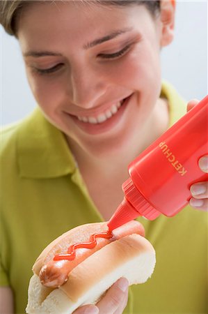 spreading sausage - Young woman putting ketchup on hot dog Stock Photo - Premium Royalty-Free, Code: 659-03529457