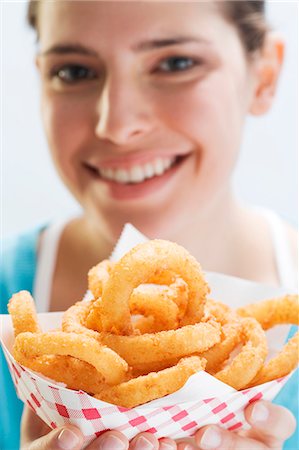 Young woman holding deep-fried onion rings in paper dish Stock Photo - Premium Royalty-Free, Code: 659-03529462