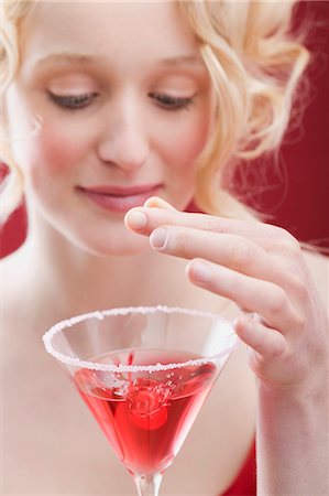 simsearch:659-07027867,k - Young woman dropping cherry into Cosmopolitan Stock Photo - Premium Royalty-Free, Code: 659-03521798