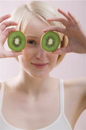 simsearch:659-01855145,k - Young woman with two kiwi fruit halves in front of her face Foto de stock - Royalty Free Premium, Número: 659-03523388