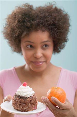 enquiring - Young woman undecided between cake and orange Stock Photo - Premium Royalty-Free, Code: 659-03523398