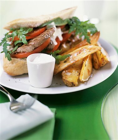 Steak sandwich with rocket, tomatoes and potato wedges Stock Photo - Premium Royalty-Free, Code: 659-03523972
