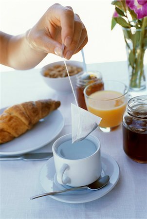 saquinho de chá - Laid breakfast table: hand holding tea bag over teacup Foto de stock - Royalty Free Premium, Número: 659-03534738