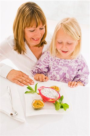 Mother and daughter sitting at table with plate of fruit Stock Photo - Premium Royalty-Free, Code: 659-03536938