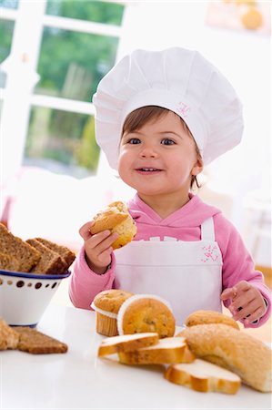 Little girl in chef's hat sitting at table with muffins Stock Photo - Premium Royalty-Free, Code: 659-03537378