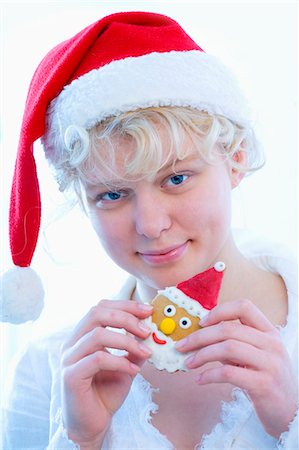 Girl in Father Christmas hat holding Father Christmas biscuit Stock Photo - Premium Royalty-Free, Code: 659-03530213