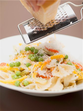 Hand grating Parmesan onto farfalle with vegetables Stock Photo - Premium Royalty-Free, Code: 659-03530487