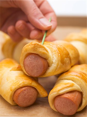 sausage recipe - Hand pushing cocktail stick into sausage roll Stock Photo - Premium Royalty-Free, Code: 659-03530519