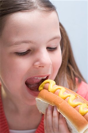 Fille de mordre dans un hot dog à la moutarde Photographie de stock - Premium Libres de Droits, Code: 659-03531196