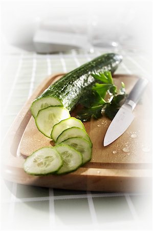 Cucumber, partly sliced, on chopping board Stock Photo - Premium Royalty-Free, Code: 659-03533642