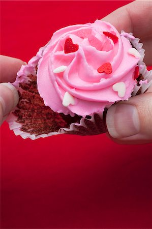 Taking chocolate cupcake with pink icing out of paper case Stock Photo - Premium Royalty-Free, Code: 659-03533839