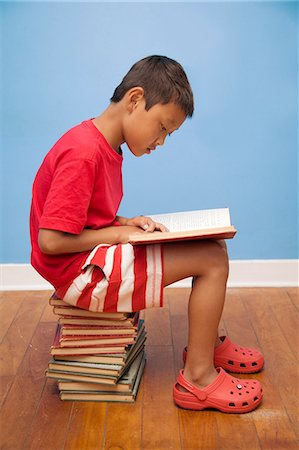 Boy reading while seated on stack of books Stock Photo - Premium Royalty-Free, Code: 673-06025504