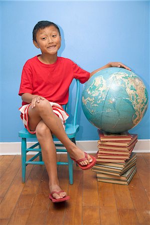 Boy seated next to globe resting on stack of books Stock Photo - Premium Royalty-Free, Code: 673-06025502