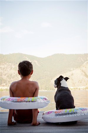 Young boy and dog wearing float rings on dock Foto de stock - Sin royalties Premium, Código: 673-06964851