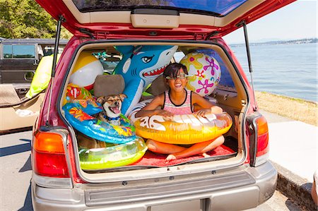 Child poses with his dog in the open trunk of a car full of beach toys and floaties Foto de stock - Sin royalties Premium, Código: 673-08139160